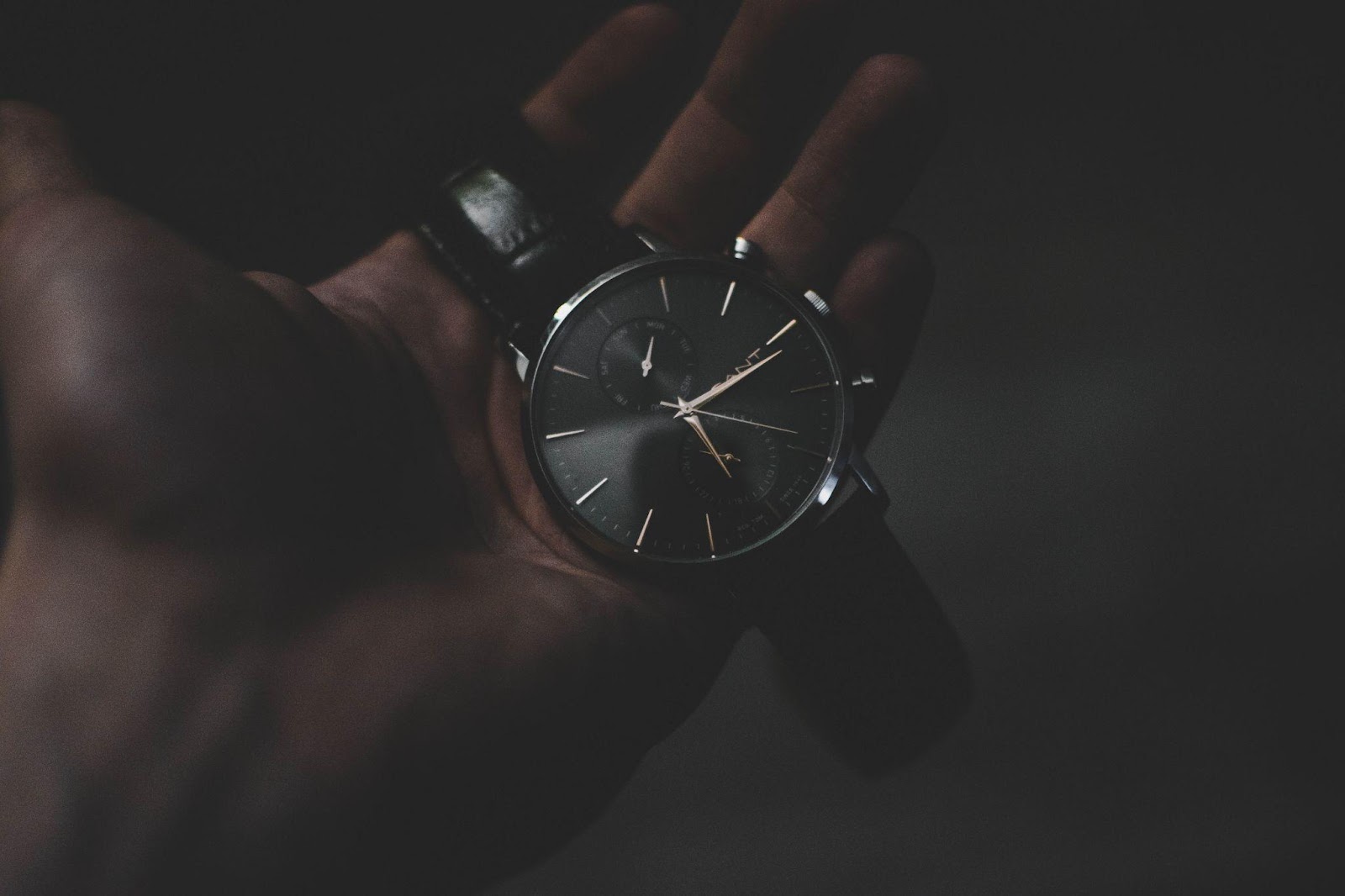 A hand holding a black dial and leather band