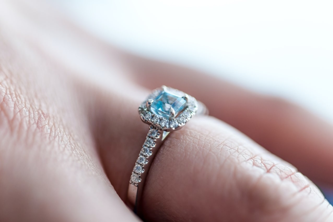 close up image of a person’s hand wearing a blue topaz engagement ring