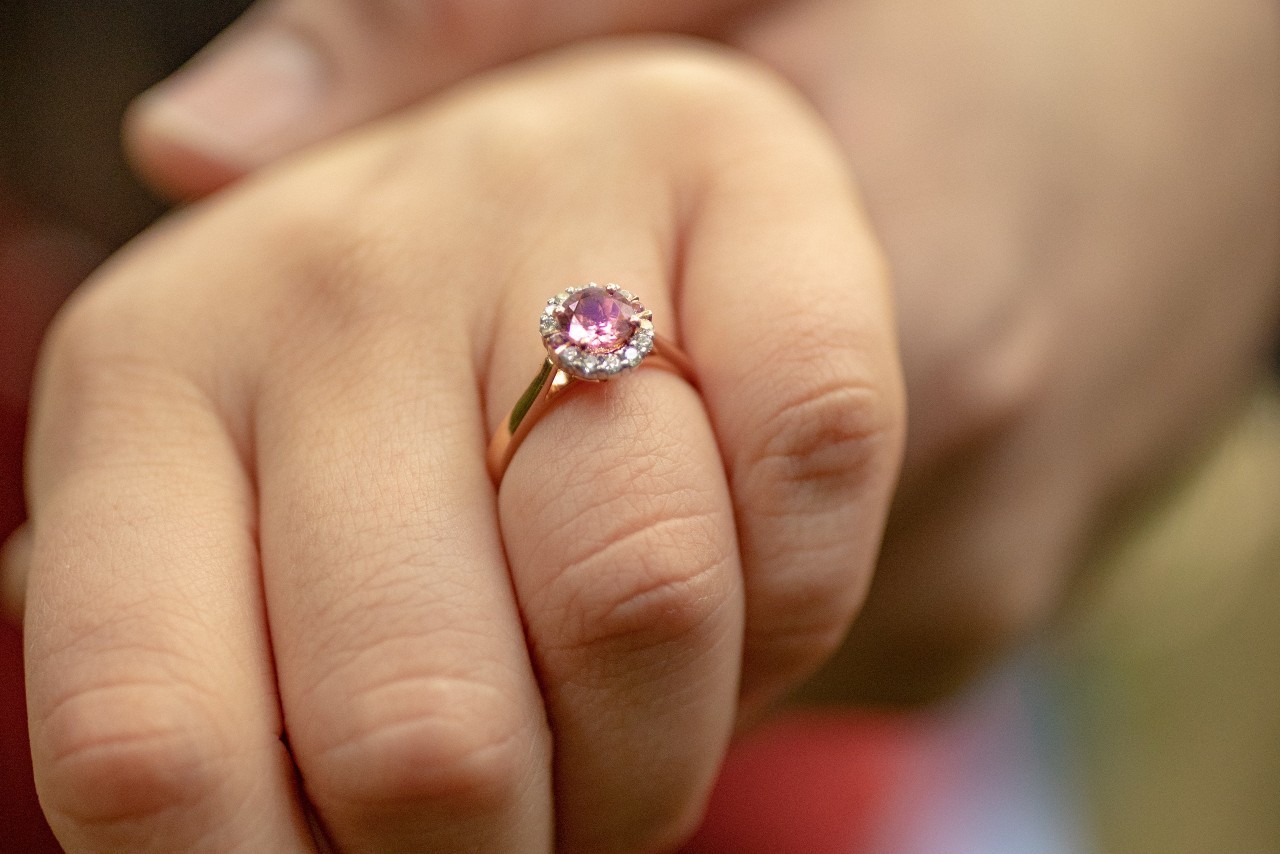 a woman’s hand adorned with a rose gold engagement ring with a pink center stone