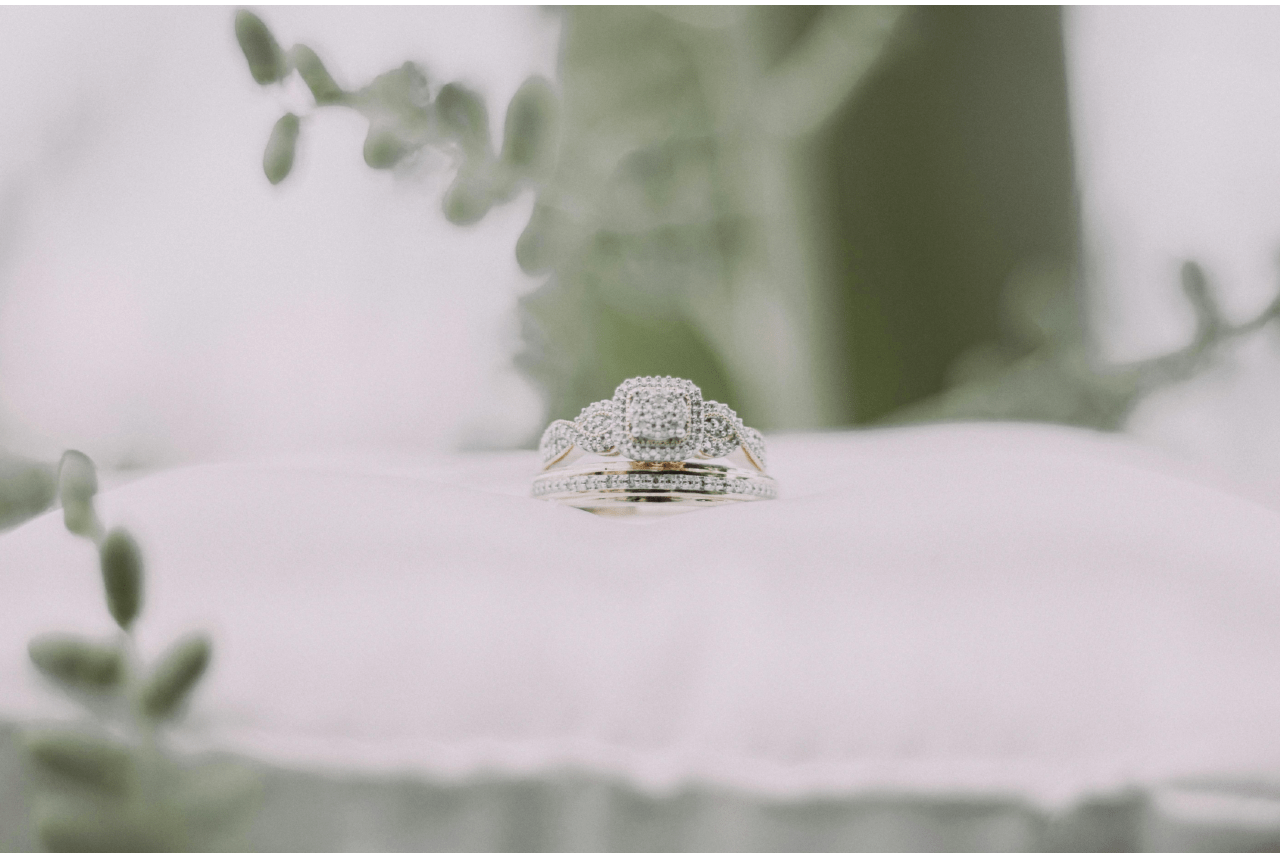 An elegant engagement ring displayed on a white cushion atop a matching wedding band.