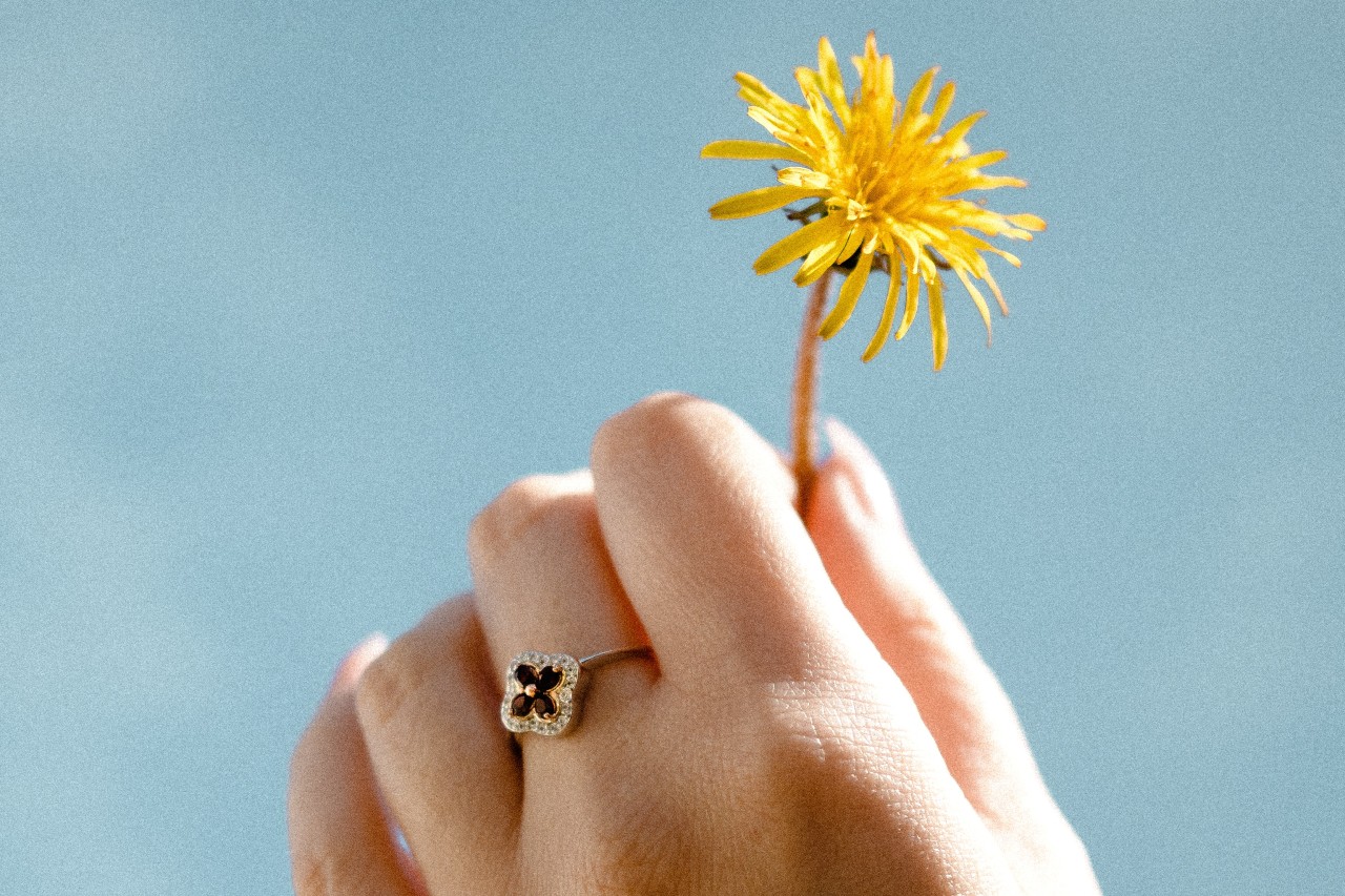 a hand holding a dandelion to the sky and wearing a floral ring