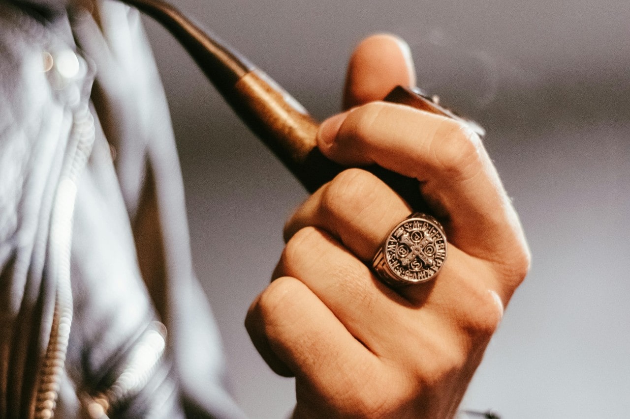 a man’s hand holding a pipe and wearing a large signet ring