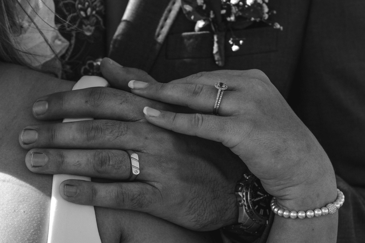 a black and white photo of a bride and groom’s hands, wearing their wedding bands.