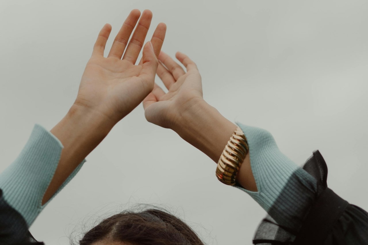 a woman’s hand raised above her head, wearing a chunky gold bracelet