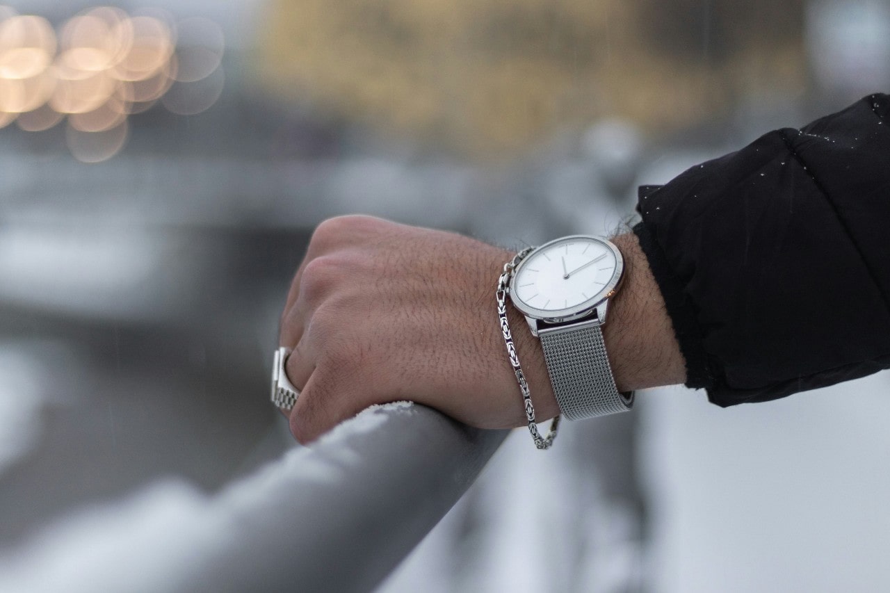 a person’s arm resting on a rail and adorned with a silver bracelet, ring, and watch