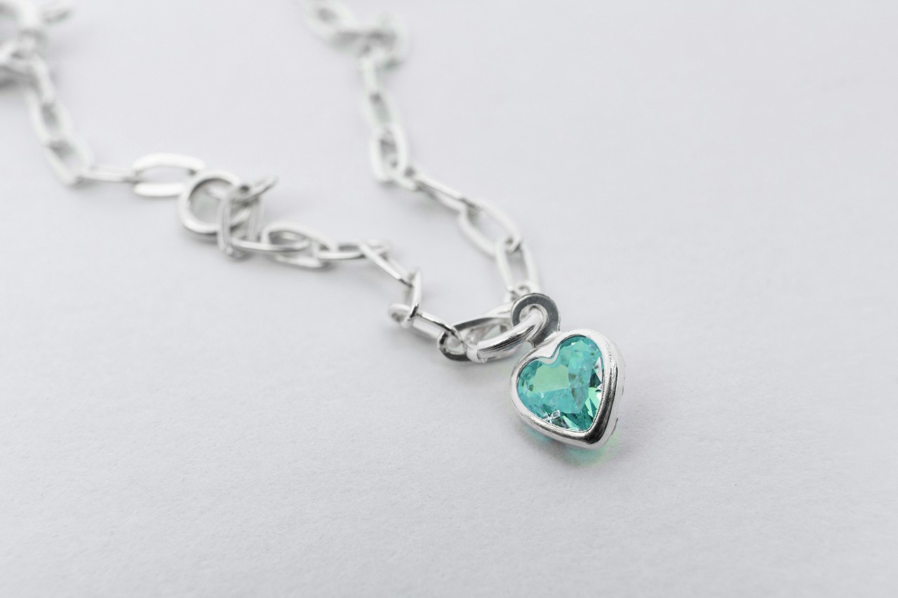 A white gold chain necklace with a blue gemstone heart pendant.