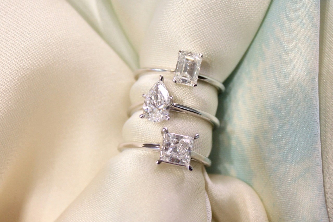 three white gold solitaire engagement rings with different diamond cuts, stacked