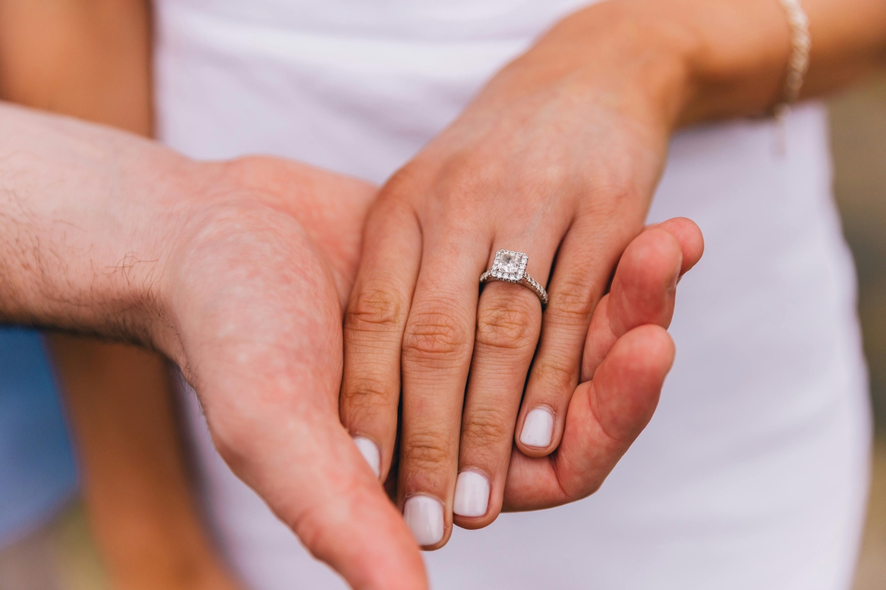 a man holding a woman’s hand, the woman wearing a princess cut halo engagement ring