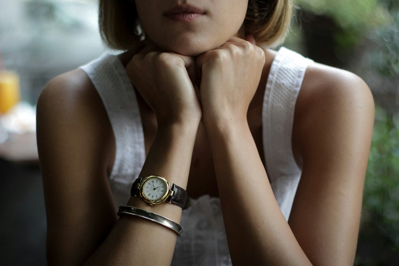 A close-up of a young woman, with emphasis on her vintage-inspired wristwatch.