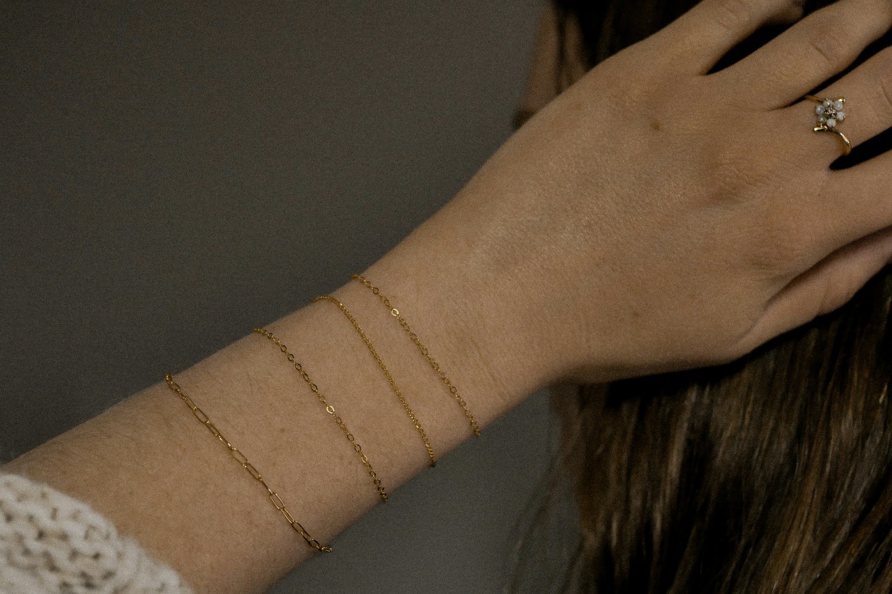 A woman’s wrist wearing four thin gold chain bracelets.