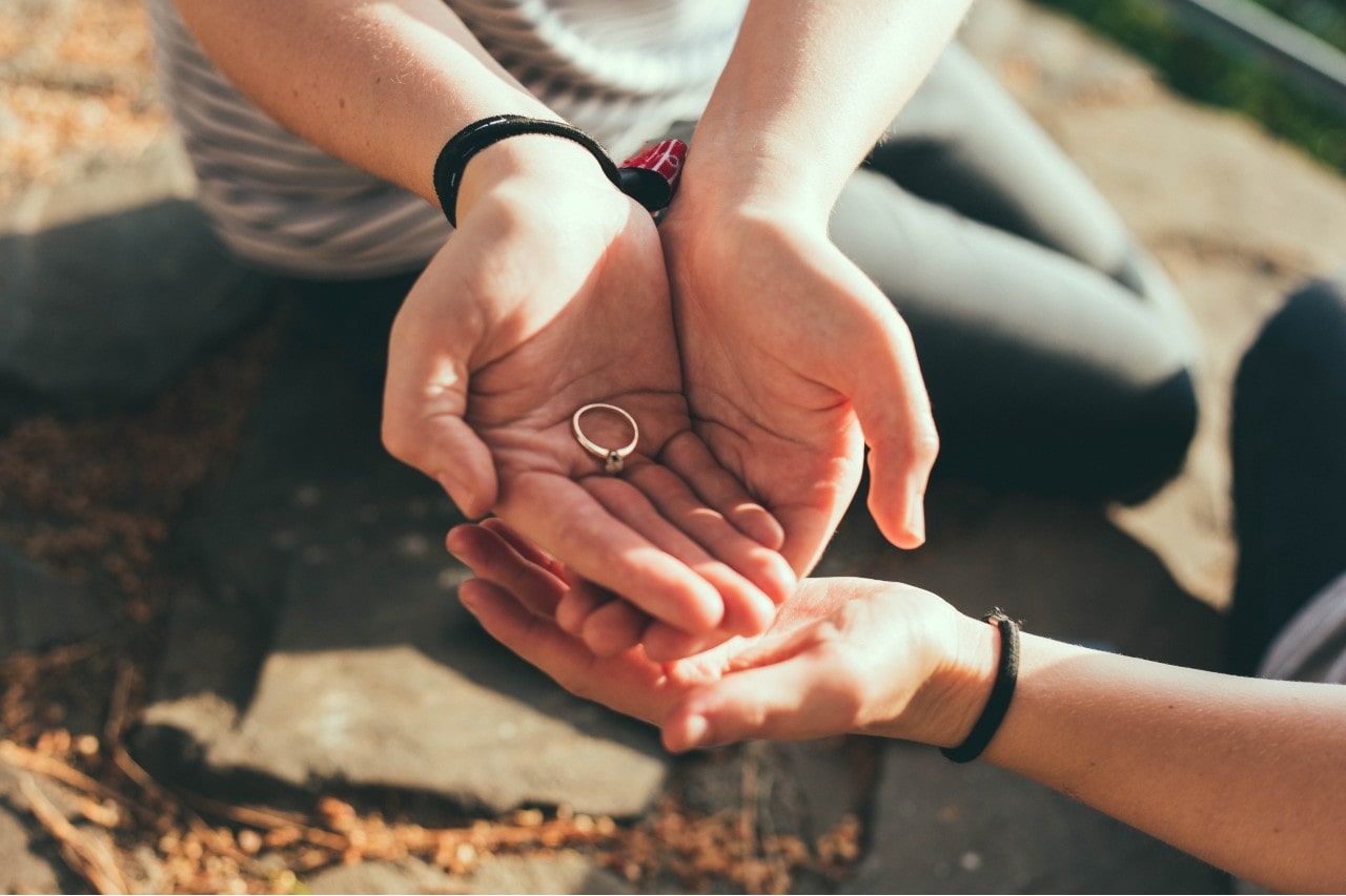 A simple silver band with a small gemstone, passed between hands in an outdoor setting