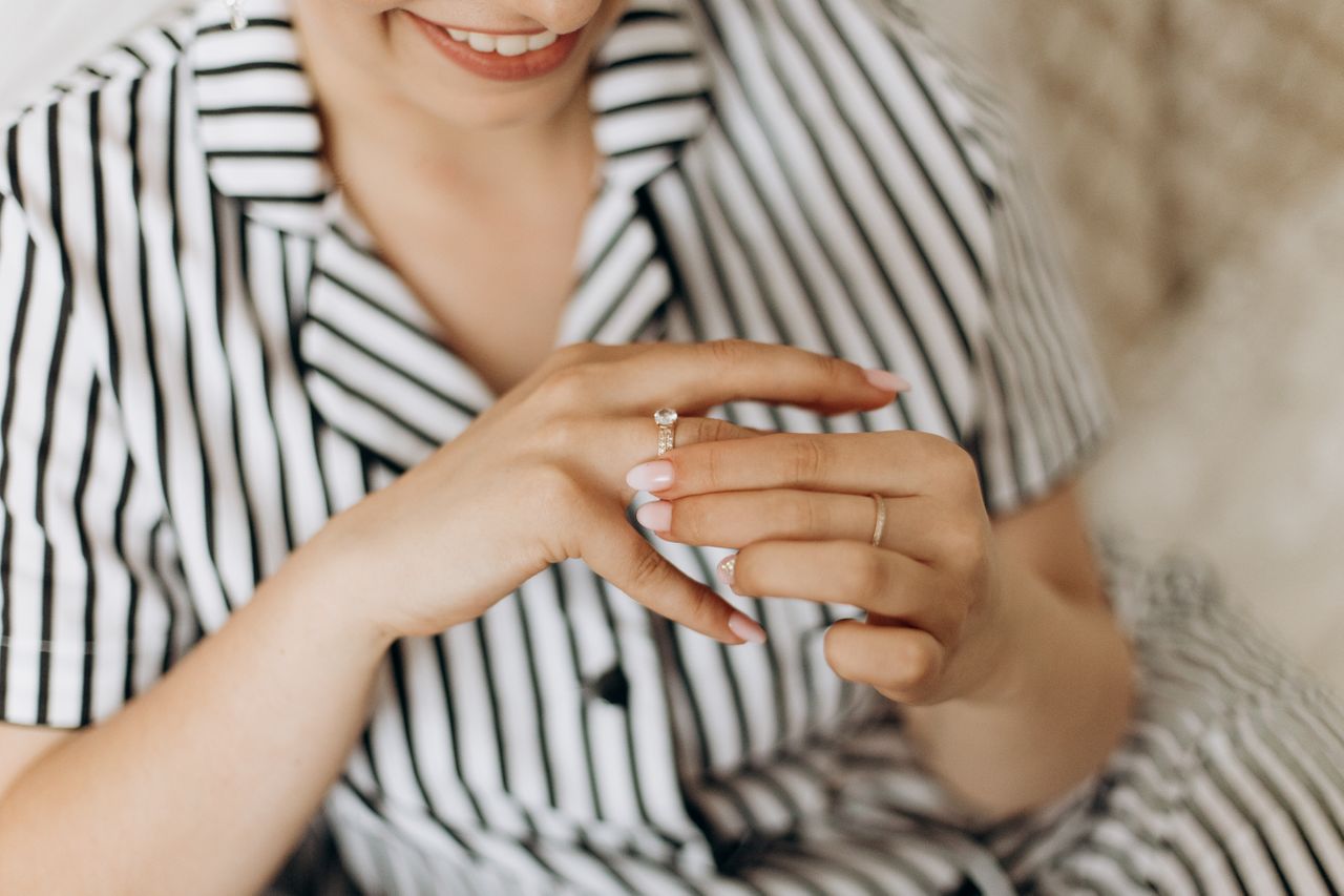 A woman wearing an elegant engagement ring with a large, sparkling diamond on a thin, delicate band