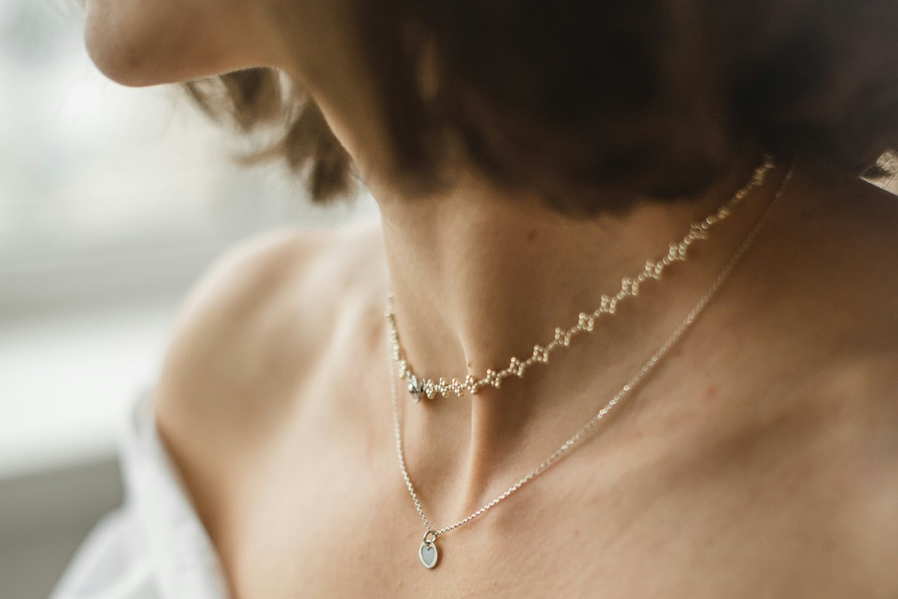 A close-up of a woman’s neck and shoulders adorned in two delicate gold necklaces.