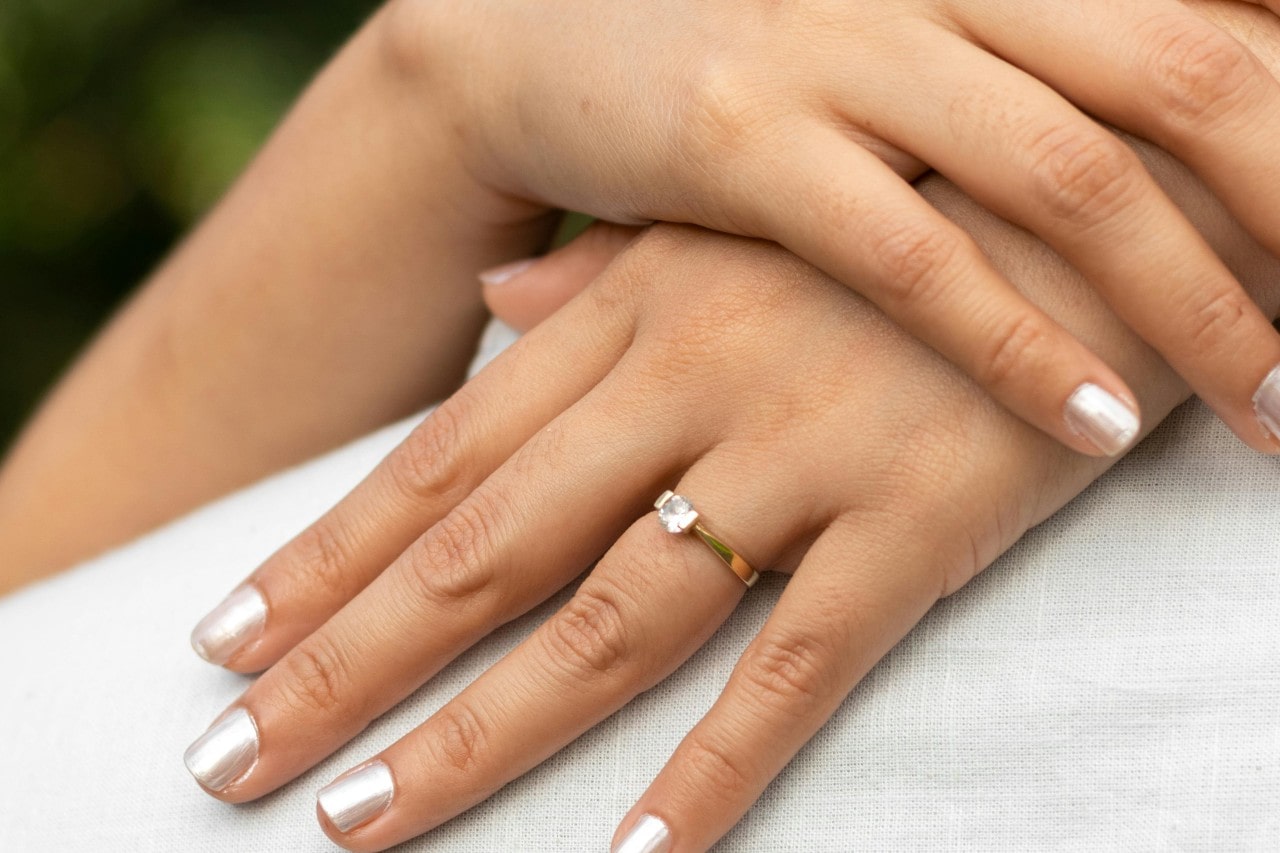 a woman’s hands on a person’s back, adorned by a solitaire engagement ring with gold band