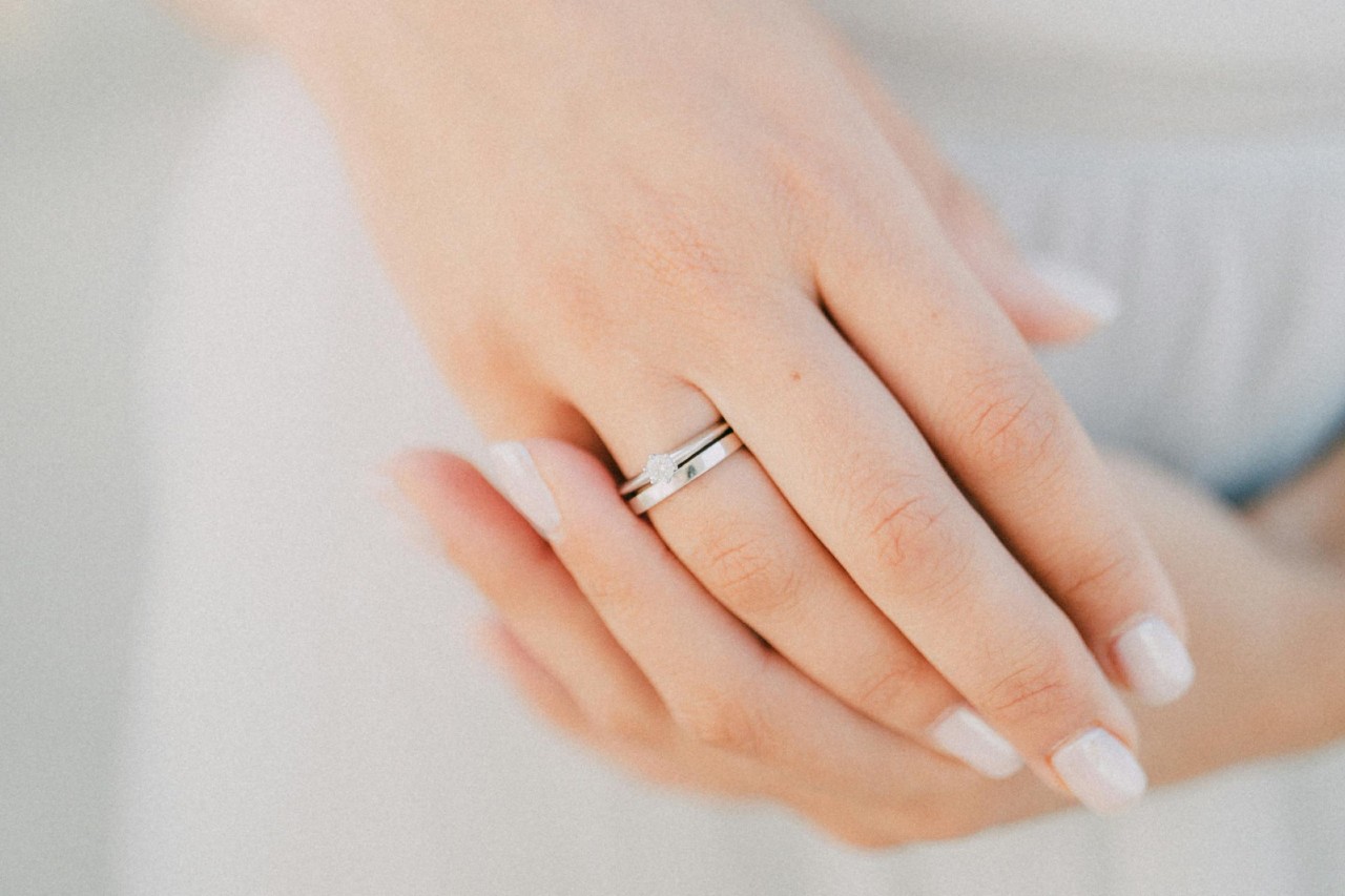 A close-up of a bride’s hands, one adorned with a simple engagement ring and wedding band.